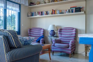 Un soggiorno con poltrone a righe, un divano, un tavolino e una libreria con libri e oggetti decorativi.