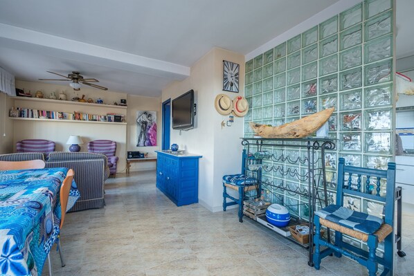 Una habitación con un armario azul, televisor, ventilador de techo y una pared con un reloj y adornos.