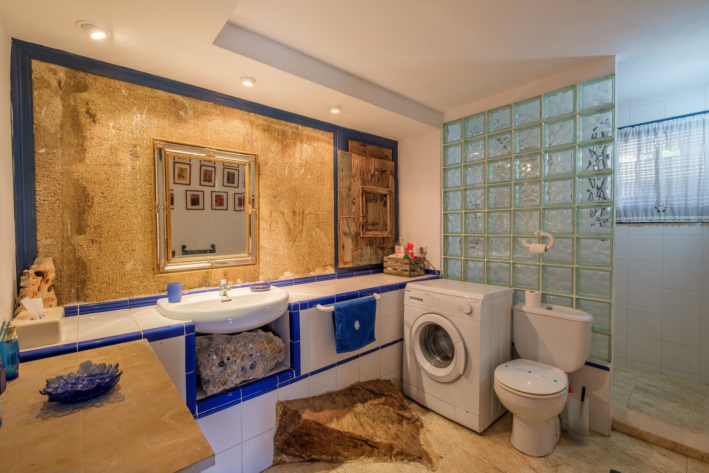 Een badkamer met een wastafel, spiegel, wasmachine, toilet en decoratieve tegels.