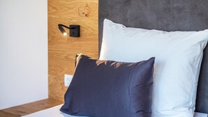 A bed with a white and dark pillow, a wooden headboard, and a wall-mounted light fixture.