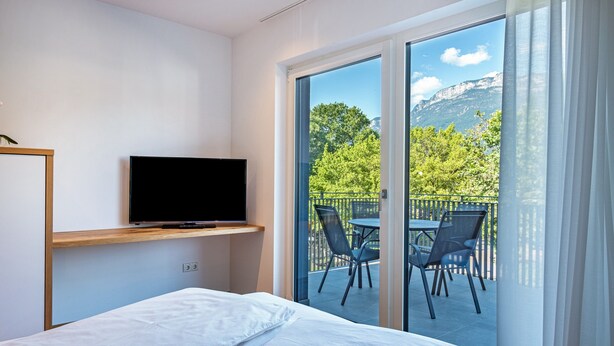 A hotel room with a bed, a TV on a shelf, and a balcony with a table and chairs.