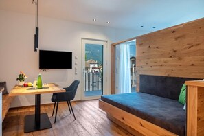 Quarto moderno com uma mesa de madeira, um sofá, uma TV fixada na parede e uma porta de vidro deslizante para uma varanda.