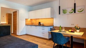 Una cocina moderna con armarios blancos, encimera de madera y una zona de comedor con una silla y una mesa azules.