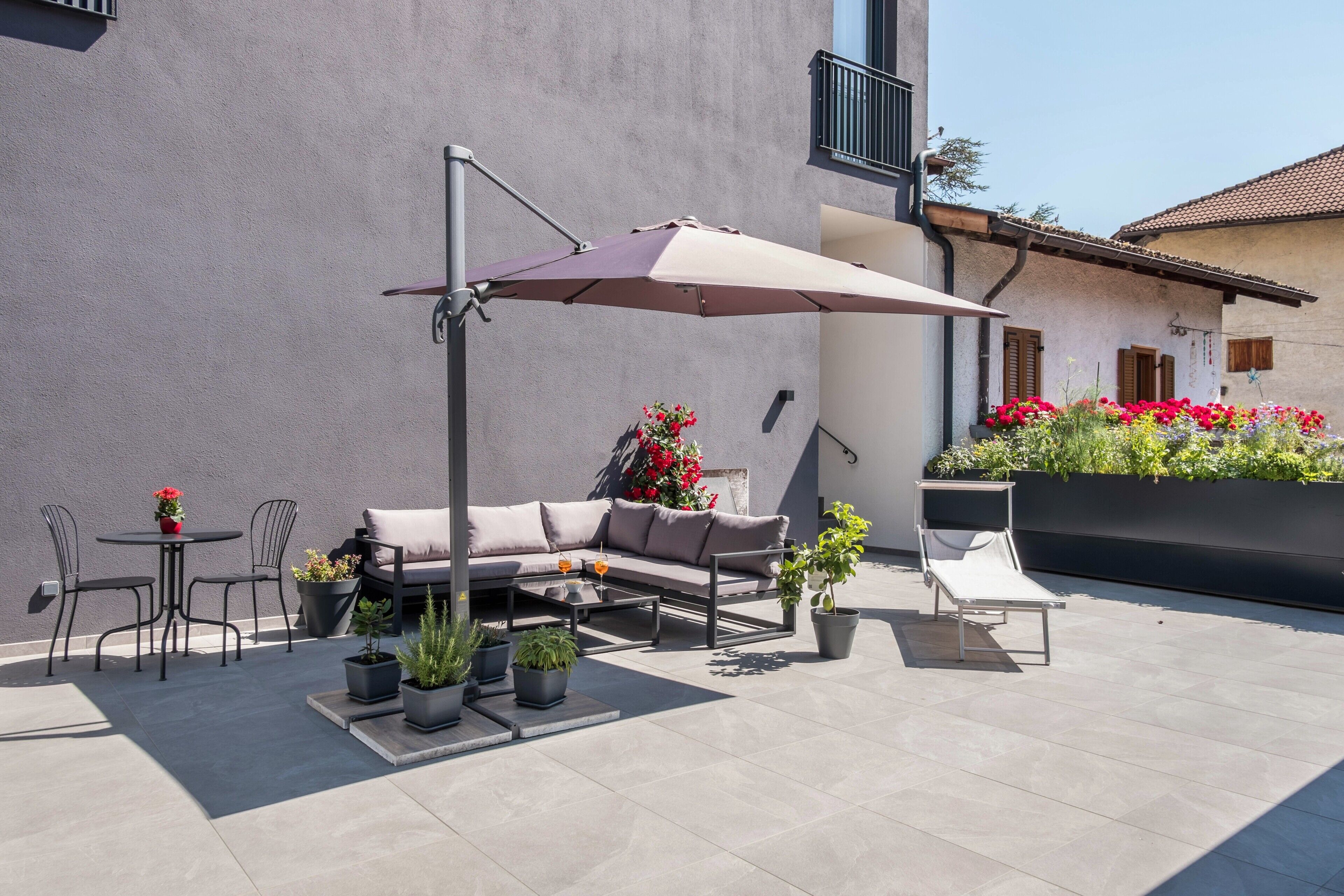 Una terrazza esterna con un divano, sedie, un tavolo, piante in vaso e un ombrellone grande.