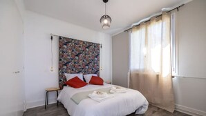 Une chambre à coucher avec un lit, une table de chevet, un luminaire suspendu et une fenêtre avec des rideaux.