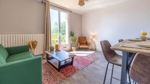 Un salon spacieux avec un canapé vert, une table basse, une table à manger avec des chaises, une lampe et une plante en pot.