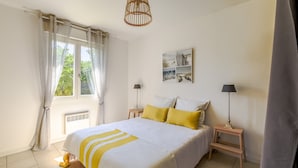A bedroom with a bed, two bedside tables, a window with curtains, a wall-mounted artwork, and a standing lamp. - Vacation Villa "Villa Teny La Teste Arcachon" with Pool, Garden, and Terrace (La Teste-de-Buch)