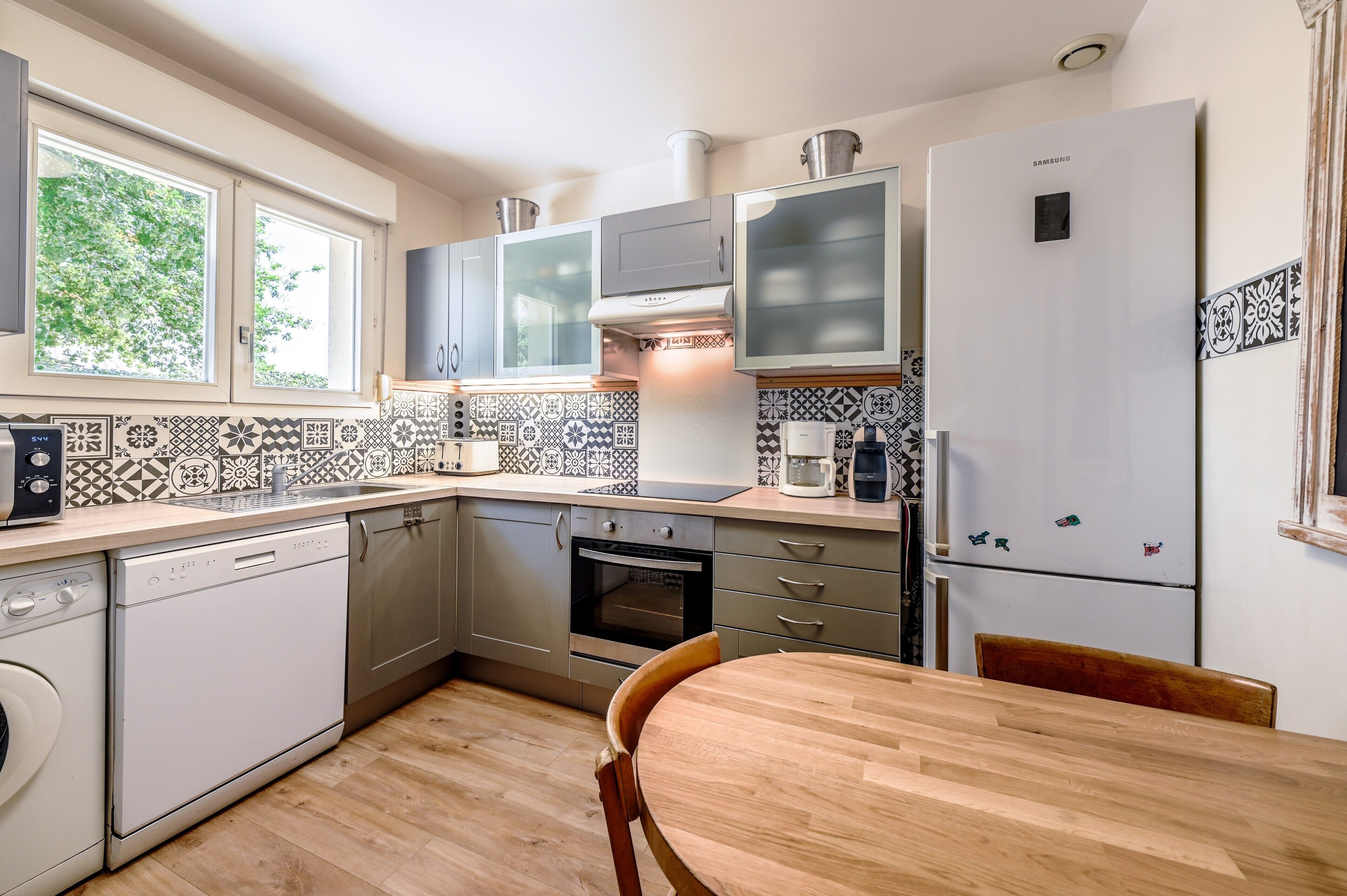 Une cuisine moderne équipée d’un lave-vaisselle, d’un four et d’un réfrigérateur, ainsi que d’une table à manger en bois et de carreaux décoratifs sur le mur derrière l’évier.