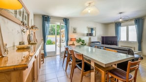 A modern kitchen with a dining area, a TV, and a large window with curtains. - Vacation Villa "Villa Teny La Teste Arcachon" with Pool, Garden, and Terrace (La Teste-de-Buch)