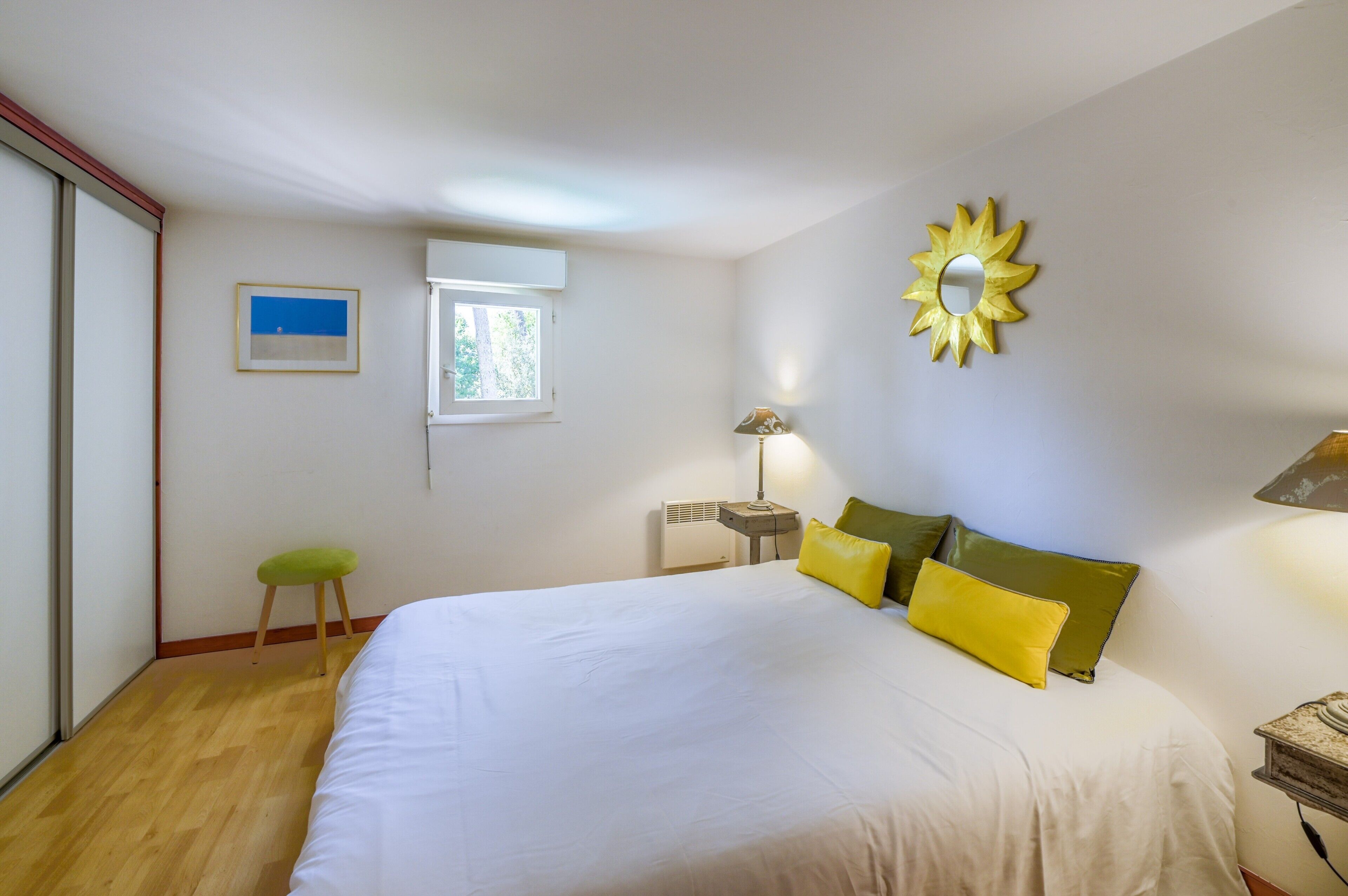 Una camera da letto con un letto, una finestra, uno specchio a muro e un piccolo sgabello.