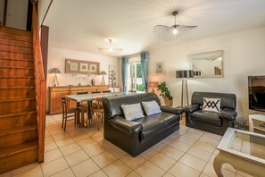 Una sala de estar con un sofá de cuero negro, una mesa de comedor y un televisor.
