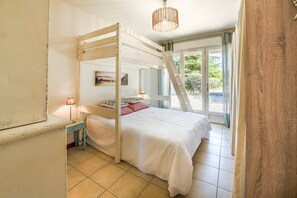 Una habitación con literas, una mesita de noche con lámpara, un cuadro en la pared y vistas a través de un ventanal.