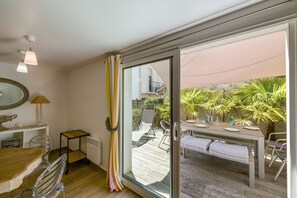 Una habitación con puerta de vidrio corredera que da a un patio exterior con mesa lista para comer, una silla y un banco.
