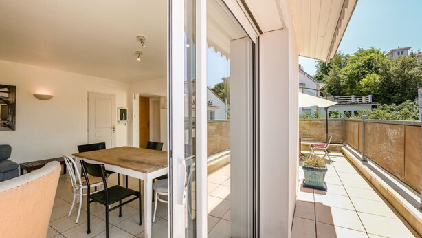 Un balcon avec une table et des chaises pour prendre les repas, une porte-fenêtre coulissante et une vue sur le quartier environnant.