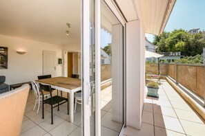A balcony with a dining table and chairs, a sliding glass door, and a view of the surrounding neighborhood.