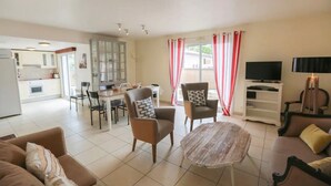 Un salon comprenant un canapé, des fauteuils, une table basse, un téléviseur et un coin repas avec des chaises et une table.