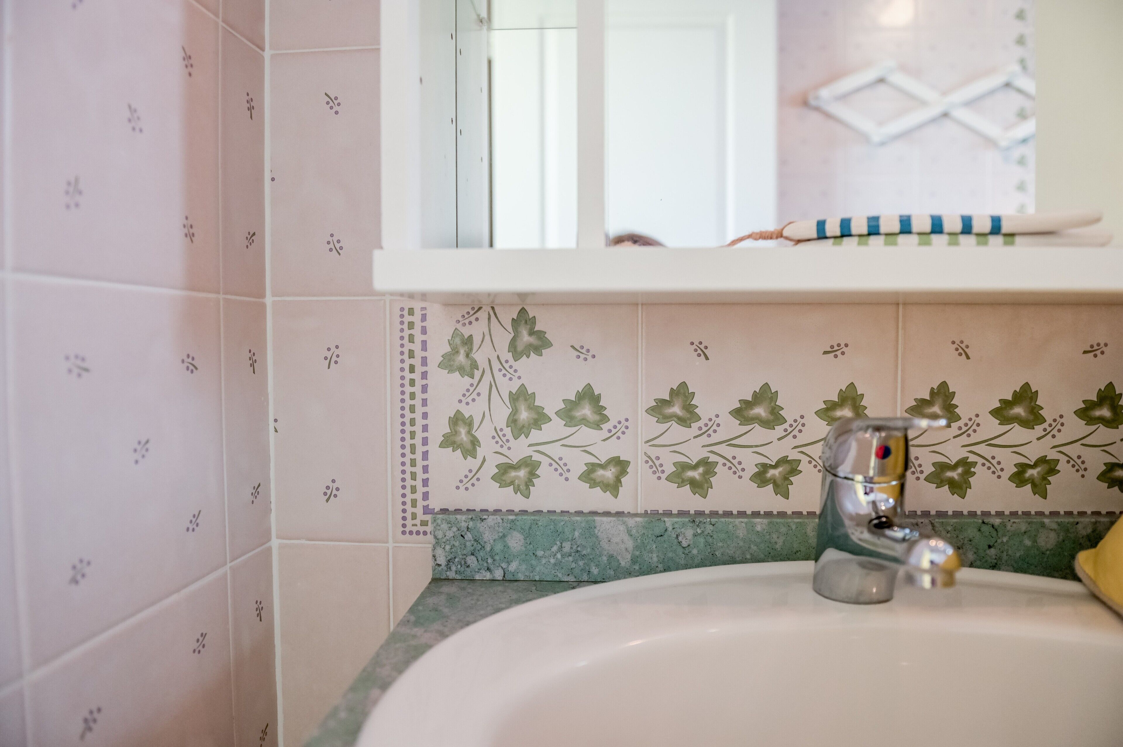 A bathroom with a sink, mirror, and decorative tiles.