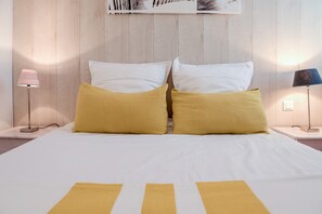 A bed with white and yellow bedding, two bedside lamps, and a wooden headboard.