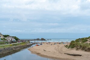 A coastal beach scene with a sandy shore, a calm sea, and a few boats. - Stylish Home with Parking, Minutes from Beach (Bude)