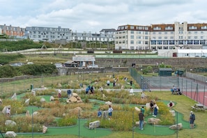 Un parcours de minigolf avec un terrain verdoyant, des rochers et quelques personnes qui jouent.