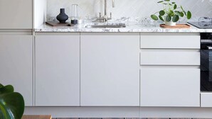 Eine moderne Küche mit weißen Schränken, einer Marmor-Spritzschutzwand und Holzboden.