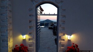 A stone archway leading to a terrace with outdoor seating and a view of the landscape.