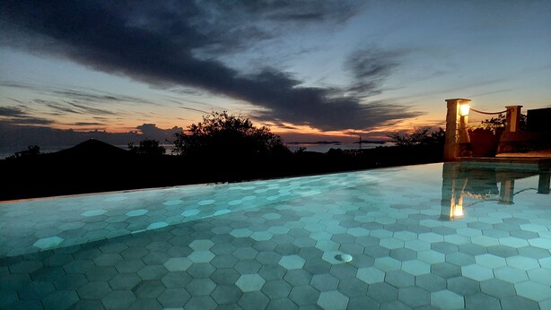 A hexagonal-tiled infinity pool with a view of a sunset over a mountainous landscape.