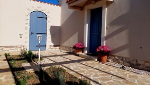 A building with a blue door and a blue arched entrance, surrounded by a stone-paved courtyard with potted plants.