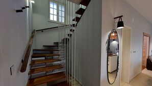A staircase with wooden steps and a glass railing, leading to a landing with a mirror and a wall-mounted light fixture.