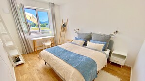 A bedroom with a bed, bedside tables, a desk, a chair, and a view of the outdoors. - Mountain atmosphere apartment - with fantastic panoramic mountain views (Garmisch-Partenkirchen)