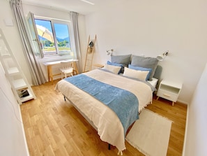 Ein Schlafzimmer mit Bett, Nachttischen, Schreibtisch, Stuhl und Blick ins Freie.