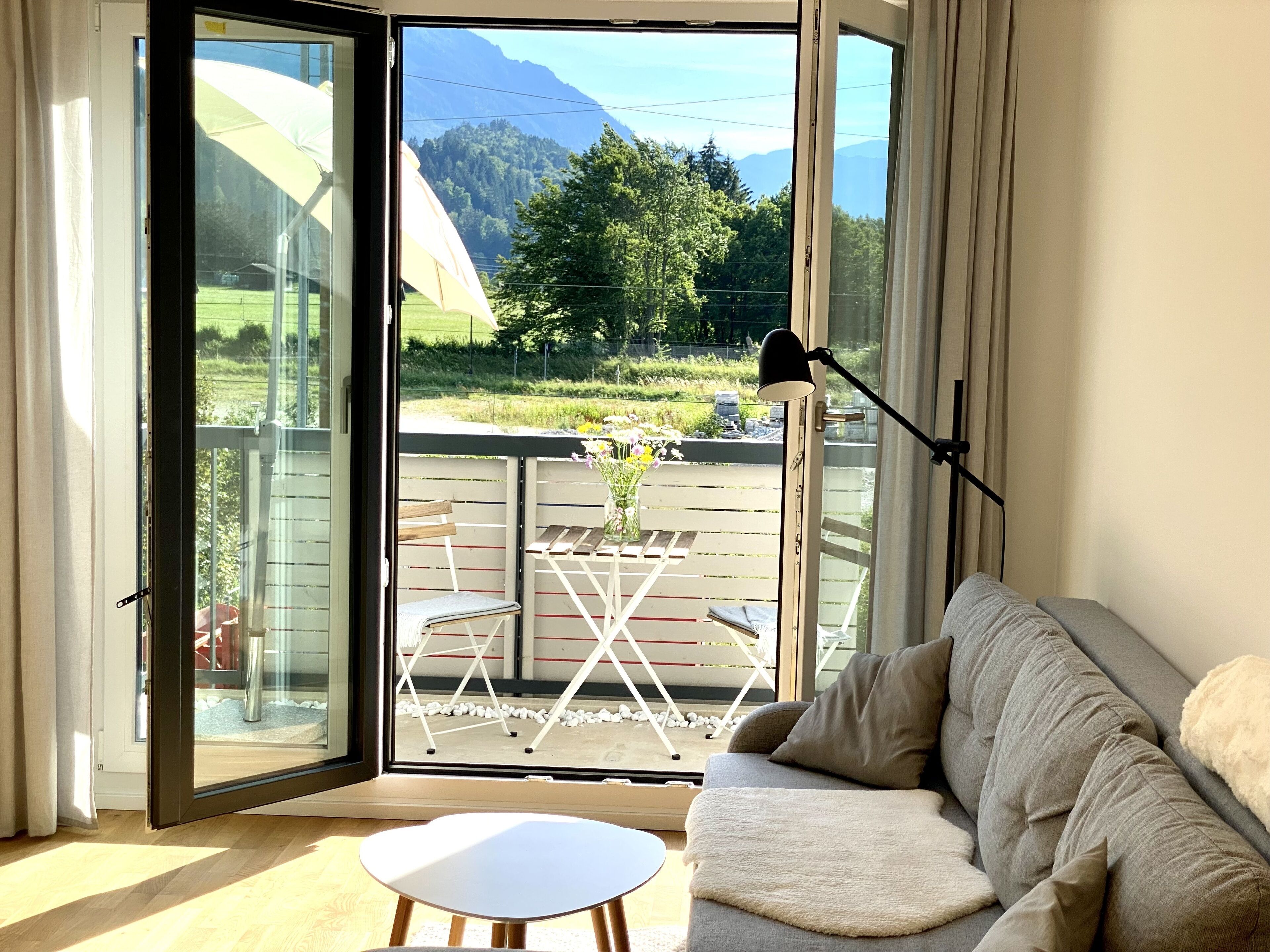 Une pièce comprenant un canapé, une petite table et donnant sur un balcon aménagé avec du mobilier d’extérieur, le tout avec une vue sur les montagnes en arrière-plan.