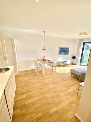 Une cuisine moderne avec une table et des chaises en bois, un petit canapé blanc et une grande fenêtre donnant sur un paysage verdoyant.