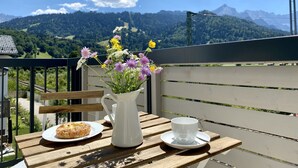 A wooden table with a white pitcher, a cup, and a plate with a pastry, set against a scenic mountain backdrop. - Mountain atmosphere apartment - with fantastic panoramic mountain views (Garmisch-Partenkirchen)