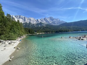 Ein klarer See mit steiniger Uferlinie, umgeben von Wald und Bergen.