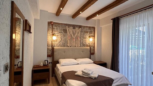 A bedroom with a bed, wooden beams, stone wall, and a window with curtains. - Gökçeada Deep Breath (Gökçeada)