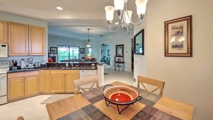 A modern kitchen with wooden cabinets, a central island, and a dining area with a table and chairs. - Sunny Punta Gorda Condo w/ Golf Course View! (Punta Gorda)