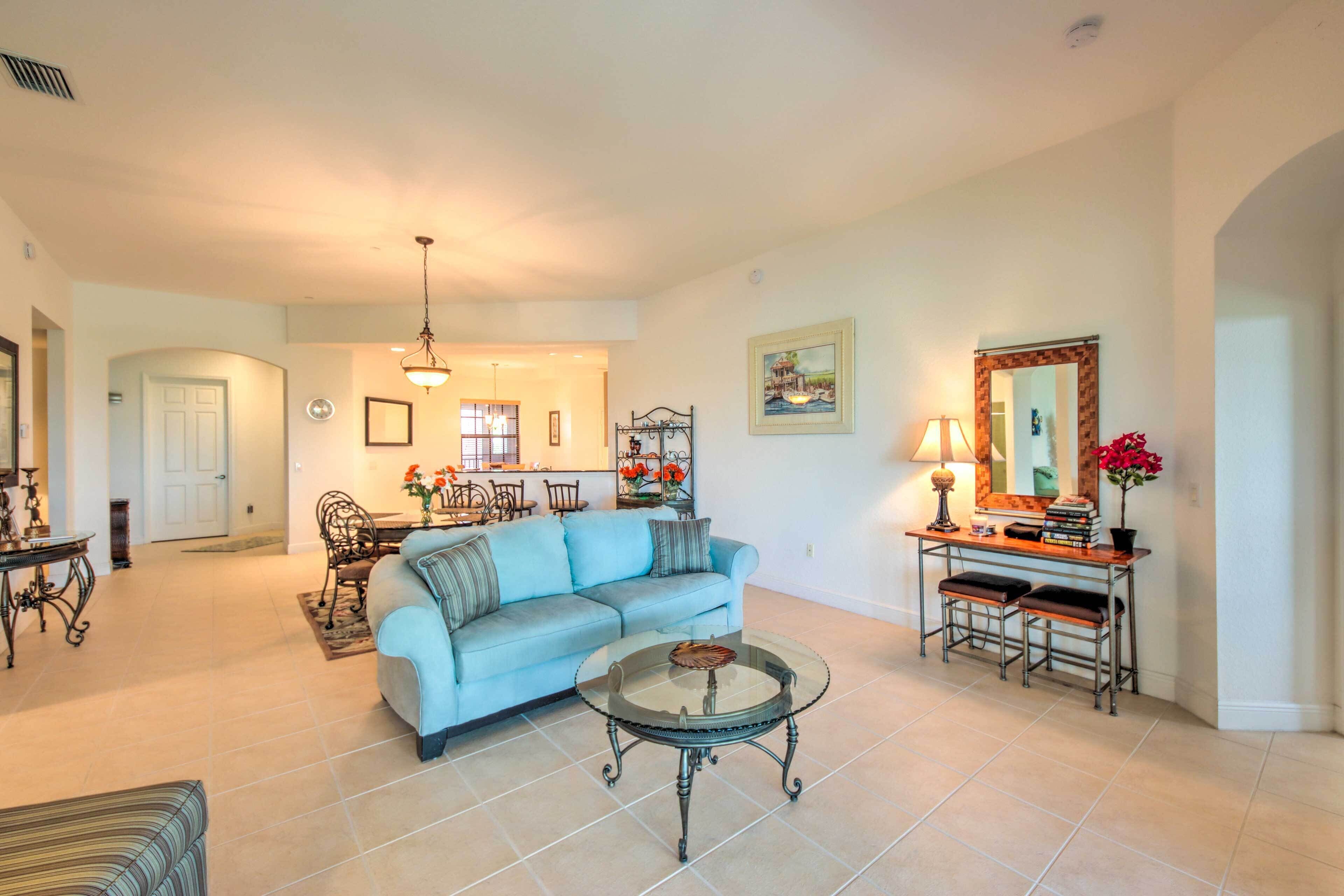 A spacious living room with a light blue sofa, a round coffee table, and a dining area with a chandelier.