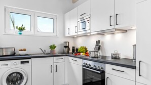A modern kitchen with white cabinets, a built-in oven, a microwave, and a washing machine. - Bajo Lykke in the North Sea resort - close to the beach and the North Sea, fireplace, infrared sauna, Terra (Büsum)