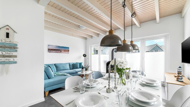 A dining area with a white table set for four, a blue sofa, and a wooden ceiling. - Bajo Lykke in the North Sea resort - close to the beach and the North Sea, fireplace, infrared sauna, Terra (Büsum)
