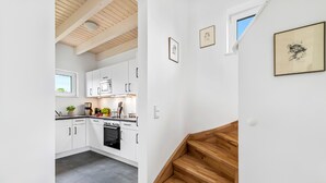 A modern kitchen with white cabinets, a built-in oven, and a wooden staircase leading to a loft area. - Bajo Lykke in the North Sea resort - close to the beach and the North Sea, fireplace, infrared sauna, Terra (Büsum)