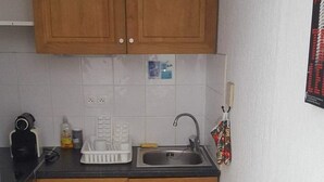Uma cozinha compacta com armários de madeira, bancada preta, pia branca e escorredor de louça. Há dois rolos de papel higiênico na bancada.