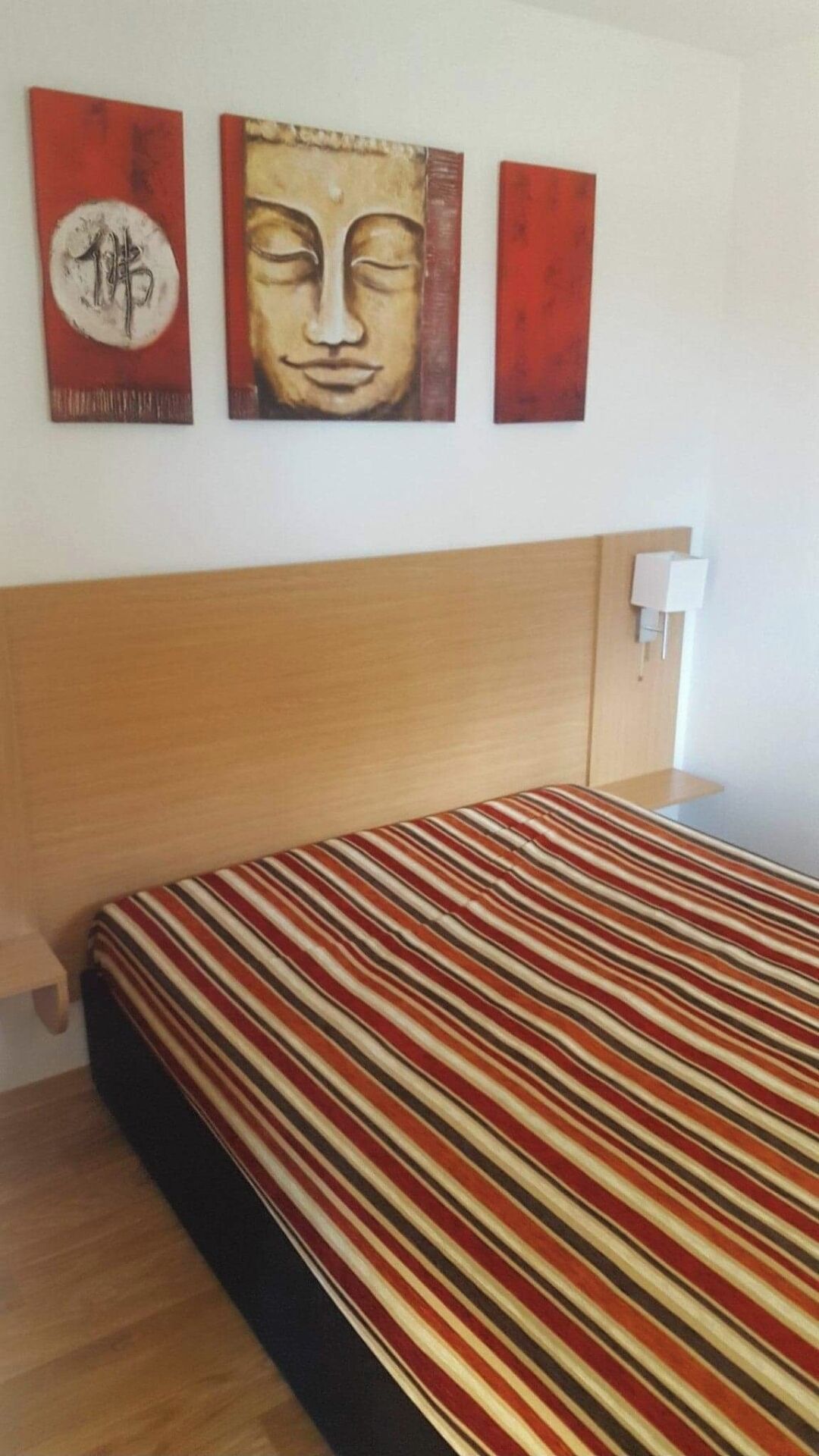 A hotel room with a wooden headboard, a striped bedspread, and three artworks on the wall.