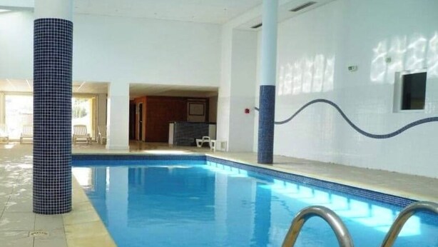 Piscina interna com água azul cristalina, paredes revestidas de azulejo e escada de metal.