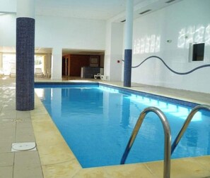 An indoor swimming pool with clear blue water, tiled walls, and a metal ladder.