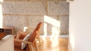 A room with a stone wall, wooden floor, a chair, and a white wall with a shelf. - Biscoito Guest House (Viana do Castelo)