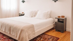A bedroom with a bed, bedside tables, a nightstand, a rug, and a wall-mounted lamp. - Biscoito Guest House (Viana do Castelo)