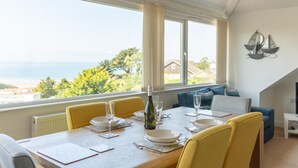 A dining area with a table set for four, a bottle of wine, and a view of the sea. - Higher Upover (Woolacombe)