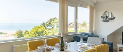 A dining area with a table set for four, a bottle of wine, and a view of the sea.