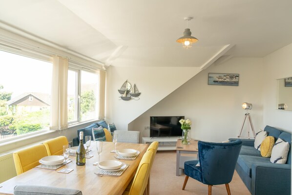 Un coin repas avec une table en bois dressée pour quatre personnes, un canapé et un téléviseur.